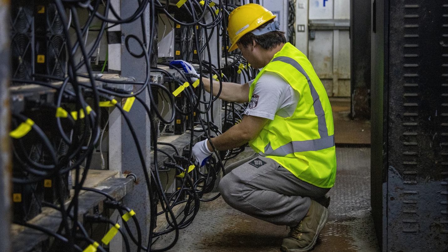 A person in a yellow hard hat working on wires
Description automatically generated